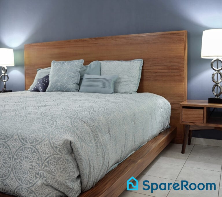 Modern bedroom with wooden bed frame and soft blue bedding representing spare room rental potential