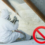 Worker spraying foam insulation in attic with red prohibition symbol