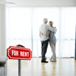 Older couple viewing rental apartment with “For Rent” sign, reflecting retirement housing challenges