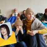 Families in a shelter eating food while facing homelessness funding cuts.