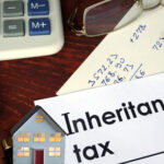 Inheritance tax paperwork with calculator, notes, and model house showing property market impact