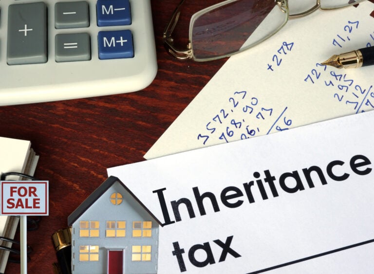 Inheritance tax paperwork with calculator, notes, and model house showing property market impact