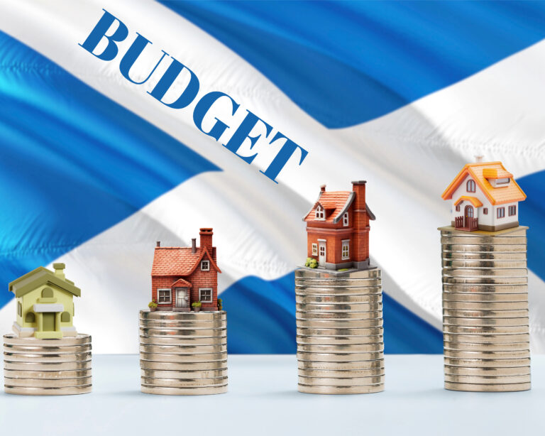 Stacked coins with model houses and Scottish flag illustrating budget impact on housing and landlords