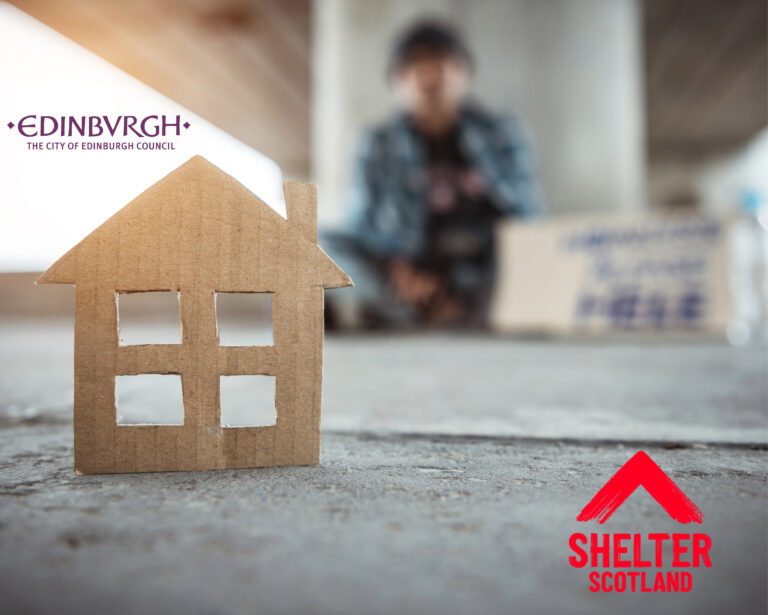 Cardboard house model with blurred homeless person in background, highlighting housing crisis in Edinburgh