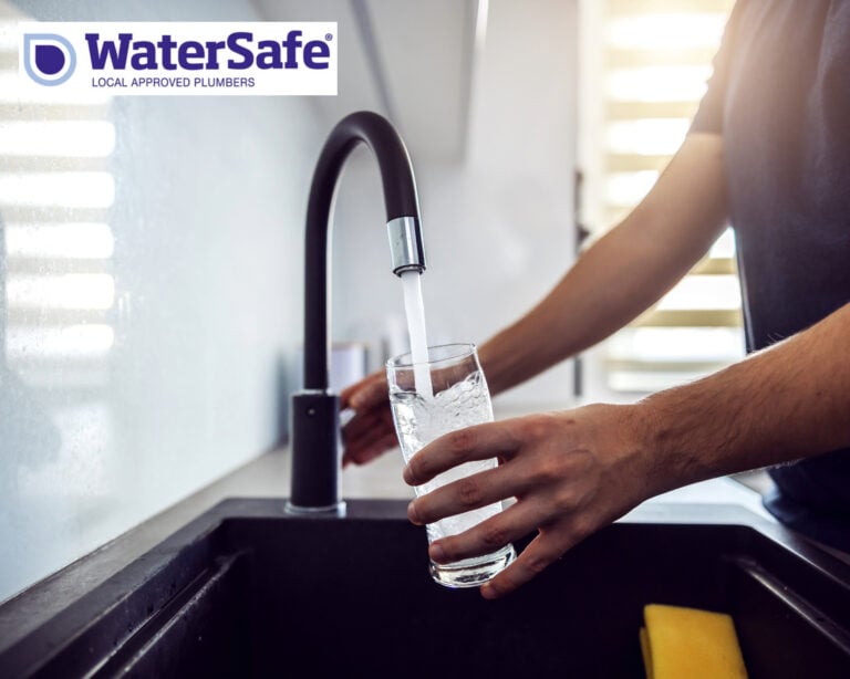 Person filling a glass of drinking water from a kitchen tap, promoting lead-free plumbing safety.