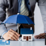 Businessman protecting house model with umbrella, symbolizing landlord insurance coverage.