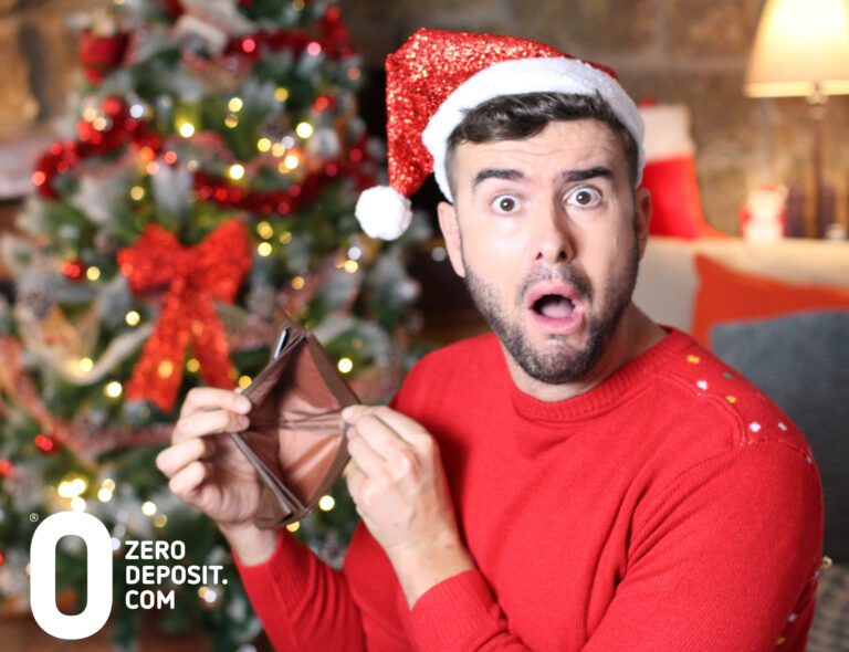 Man in Santa hat shocked by empty wallet in front of Christmas tree