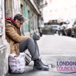 Homeless man sitting on a London street holding a cup, highlighting homelessness crisis