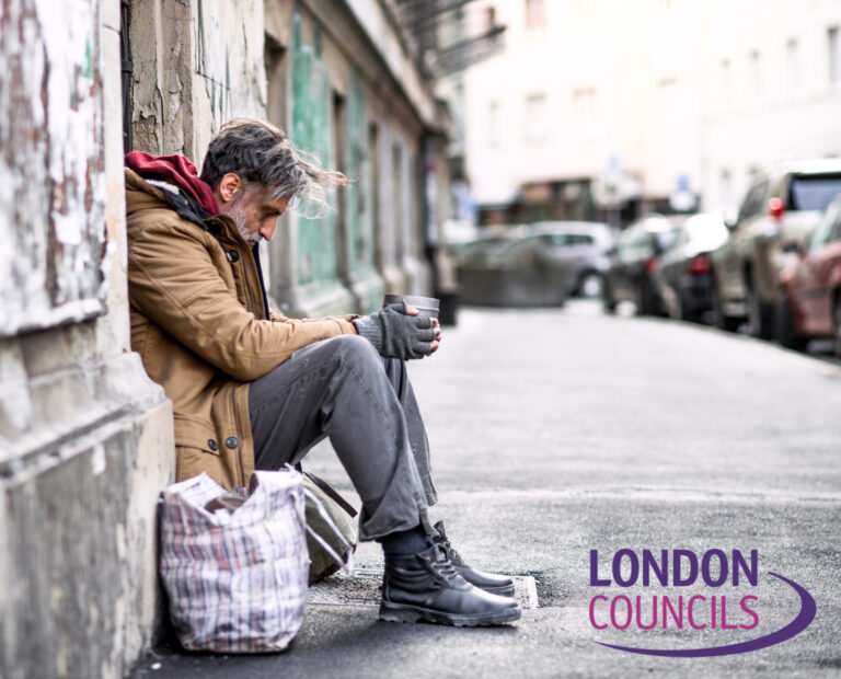 Homeless man sitting on a London street holding a cup, highlighting homelessness crisis