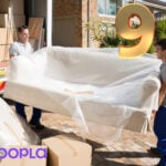 Movers carrying a wrapped sofa into a house with boxes around