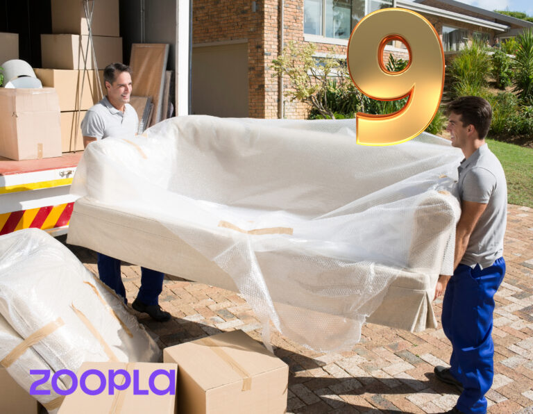Movers carrying a wrapped sofa into a house with boxes around