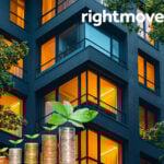 Stacks of coins with plants growing in front of modern office building symbolizing commercial property growth