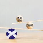 Wooden balance scale with rent control and changes, supported by a Scotland flag sphere.