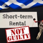 Sign reading “Short-term Rental” with keys and “Not Guilty” stamp beside Scottish flag