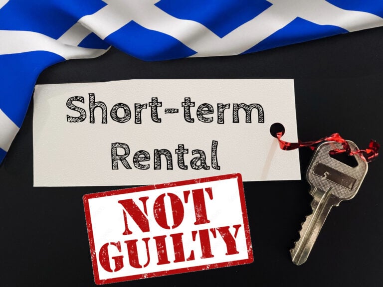 Sign reading “Short-term Rental” with keys and “Not Guilty” stamp beside Scottish flag