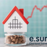 House model on coin jar with market trend graph, symbolising UK house price stability.