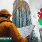 Construction worker reviewing building plans in front of high-rise with Welsh flag