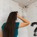 Woman looking at mould on flat wall with question mark symbol.