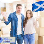 Confused couple with moving boxes and Scottish flag, highlighting tenant issues in Scotland’s rental sector