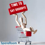 Wooden mannequin in a shopping trolley holding a red “Time to Say Goodbye” sign.