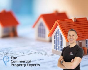 Smiling commercial property expert in front of model houses with The Commercial Property Experts logo
