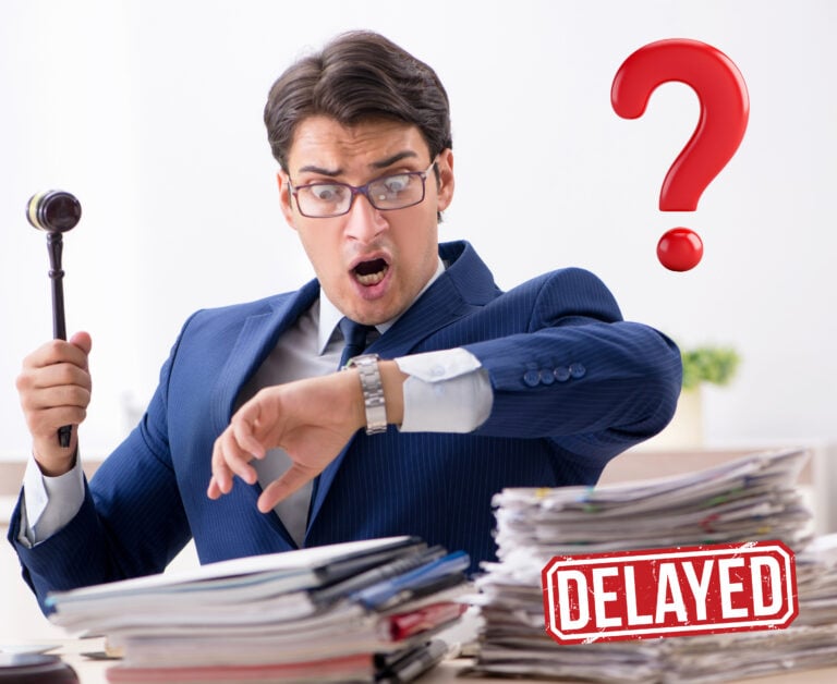 A person holding a justice hammer sitting at desk with stacked papers, a qiuestion mark and delayed sign