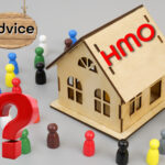 Multi coloured small figures surrounding a wooden model house with HMO on the roof and a red question mark