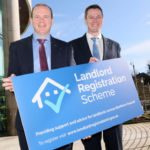 Two men holding Landlord Registration Scheme sign in Northern Ireland.