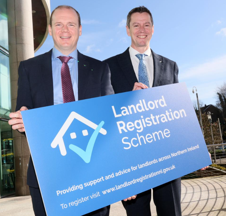 Two men holding Landlord Registration Scheme sign in Northern Ireland.