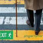 An elderly person crossing the road with a stick. Exit