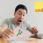 A man sitting at a desk holding papers with an arrow pointing upwards, a laptop and Savills logo