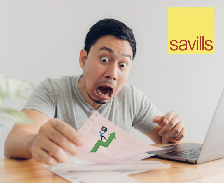 A man sitting at a desk holding papers with an arrow pointing upwards, a laptop and Savills logo