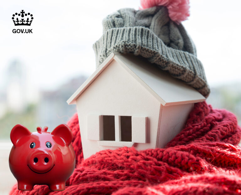 A wooden model home on a red scarf and a hat on the roof, alongside a red pig