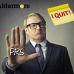 A man with his hand up in front of him, PRS and I quit on a post it note,