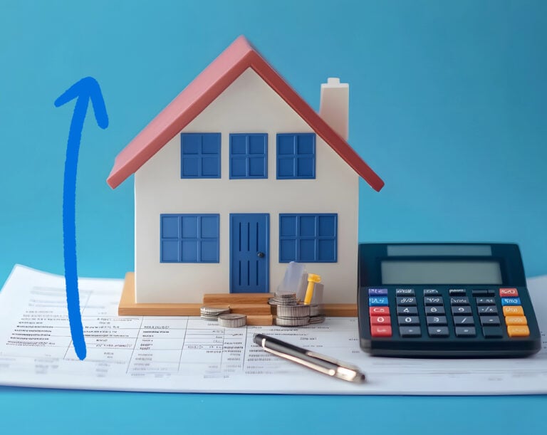 A model house, a blue arrow pointing upwards, a calculator, pen sitting on papers with a blue background