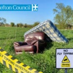 A mattress and leather armchair dumped in a field with a yellow warning no fly tipping sigh