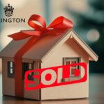 A wooden model house with a bow and a sold sign