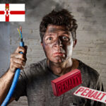 A person with smoke ash on their face, holding a cut electrical wire, penalty sign and Northern Ireland flag