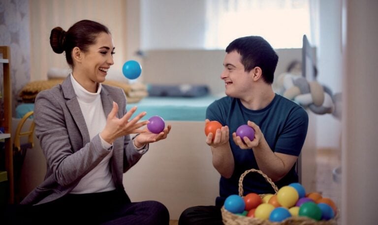 Two people sitting on a couch thrown multi coloured balls in the air and catching them