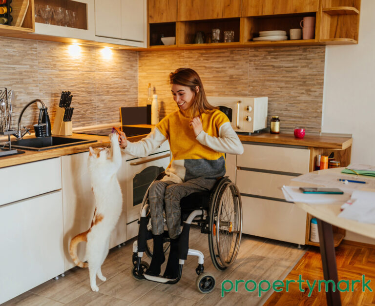 A women in a wheelchair and cat reaching up towards her in a kitchen