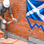 A construction working building a wall, a Scottish flag and a blue arrow pointing downwards