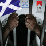 A person behaind bars in a prison with the Scottish Flag