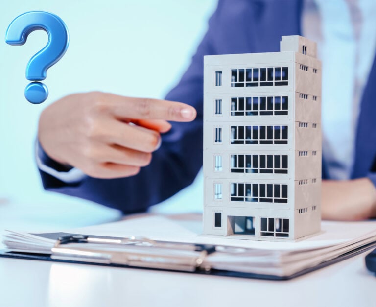 A commercial high-rise property sitting on a clipboard with a person pointing towards it and a blue question mark sign