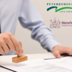 Businessman stamping official papers, Peterborough and Mansfield logos.