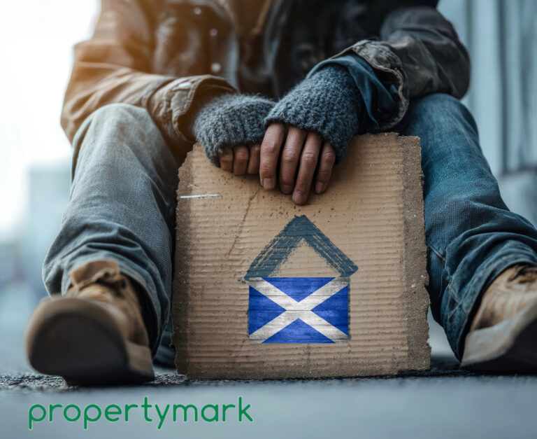 A homeless person sitting down holding a piece of cardboard with a Scottish flag