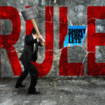 A person with a sledge hammer hitting a wall with the words RULE and short term lets