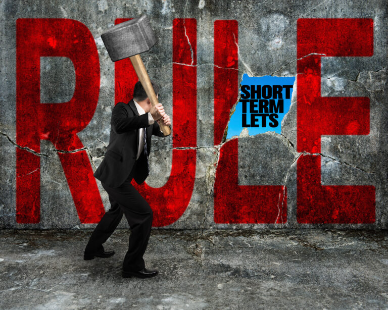A person with a sledge hammer hitting a wall with the words RULE and short term lets