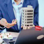 Buisnessman with a laptop holding office block for sale with a location map on the desk
