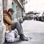 Man sitting on a city street holding a cup, highlighting homelessness in England