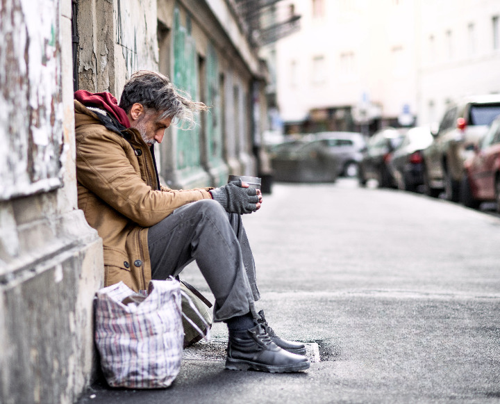 Man sitting on a city street holding a cup, highlighting homelessness in England